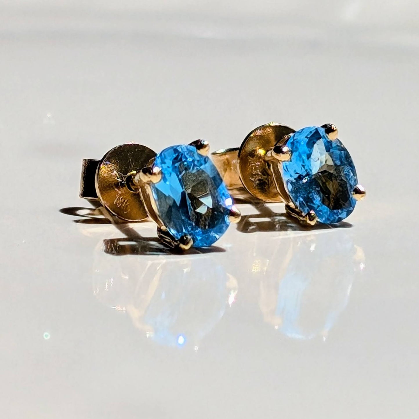 Pair of gold earrings with blue topaz gemstones on a reflective surface