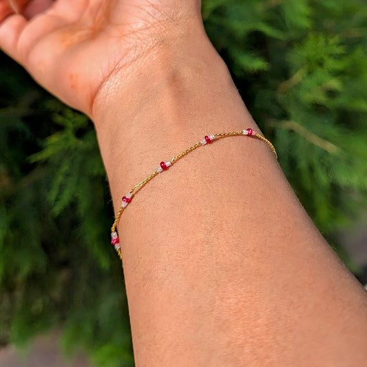 14K gold and designed for effortless everyday wear. At its centre sits a polished ruby bead, glowing with rich red intensity, flanked on either side by sparkling white diamonds.