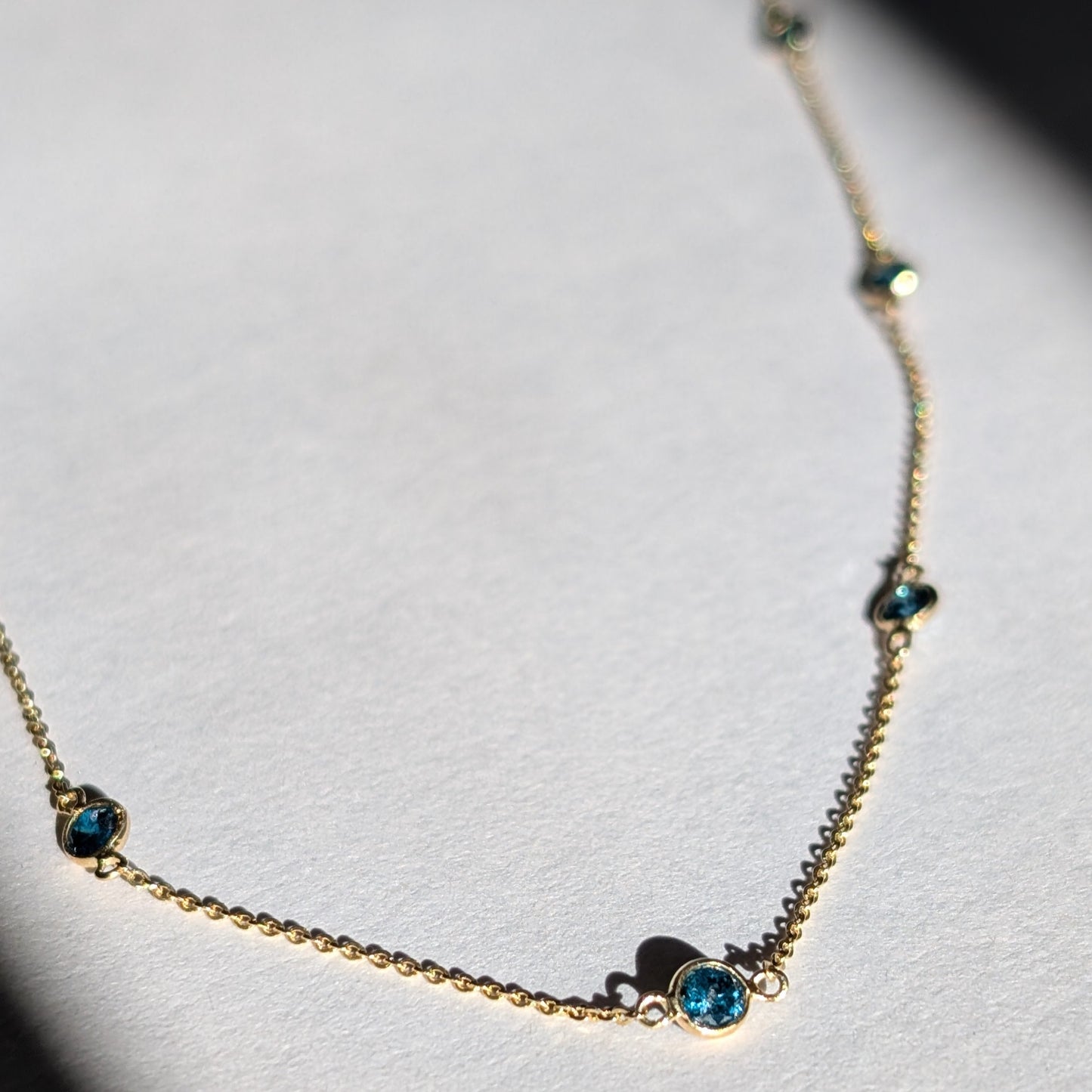 A 14K gold necklace with a series of small blue diamonds set along a longer-length chain.