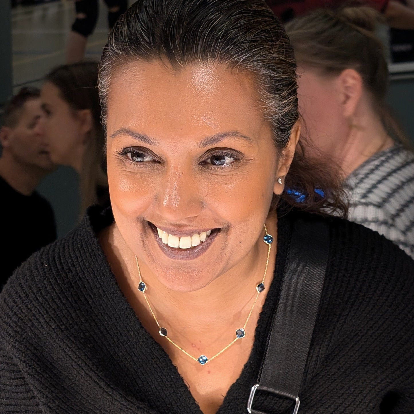 Woman wearing a black sweater wearing London Blue Topaz Necklace with a Prada pouch over her shoulder, smiling.