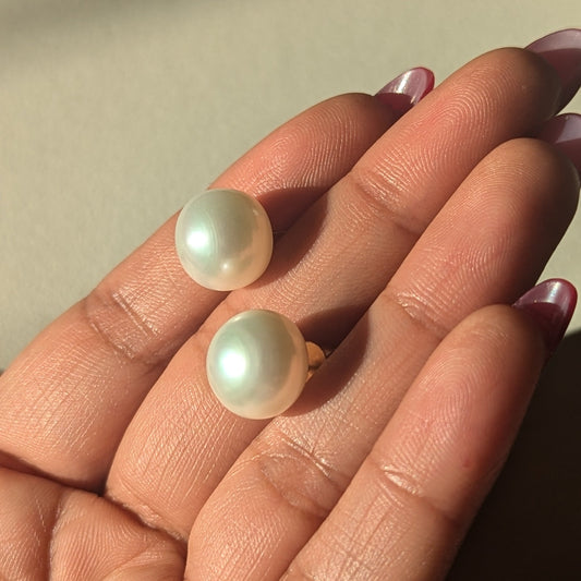 Pearl earrings held on a hand against a neutral background