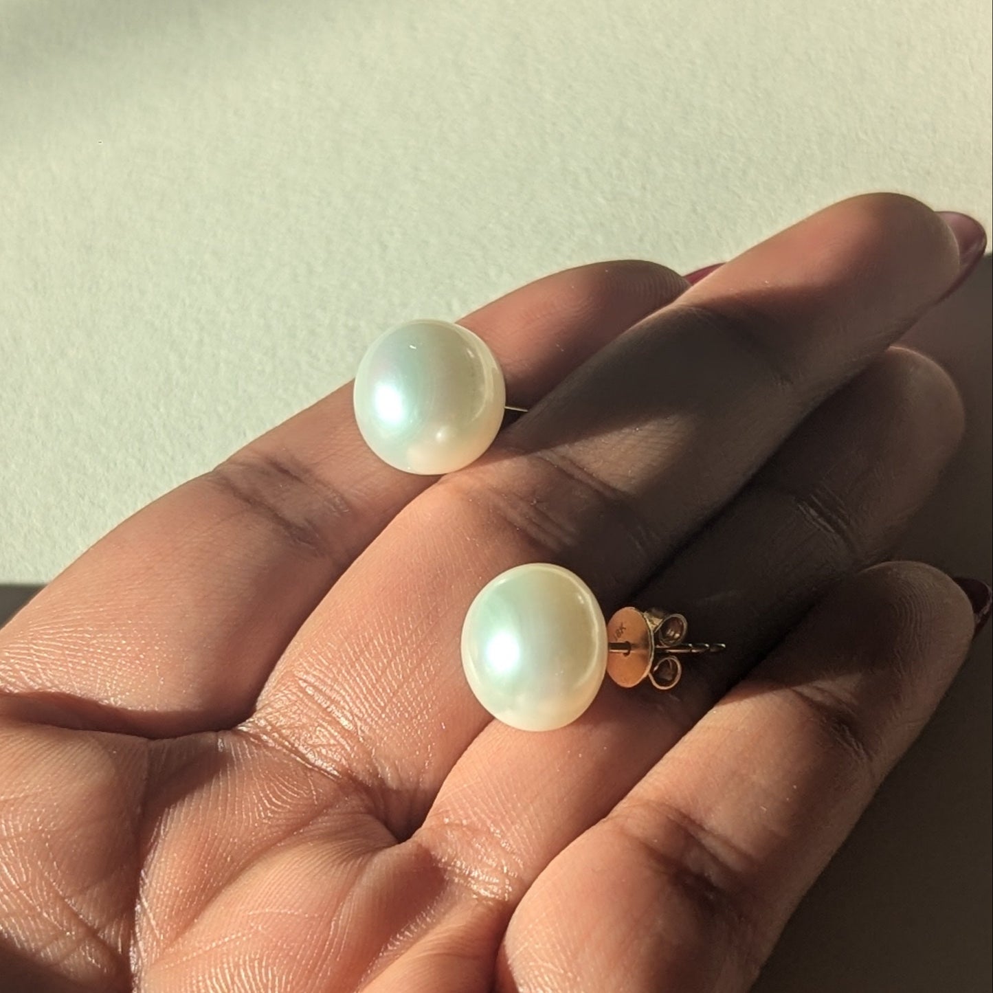 Pearl earrings held in a hand against a neutral background