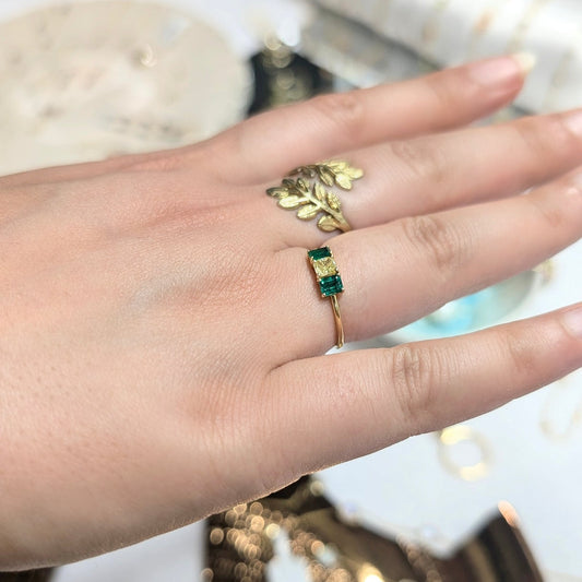 Hand wearing a green gemstone ring with gold accents on a reflective surface.