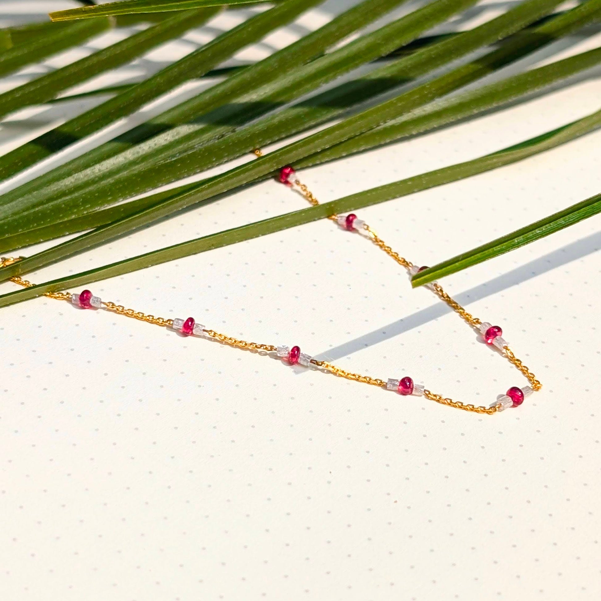 Gold necklace with red beads on a leafy background