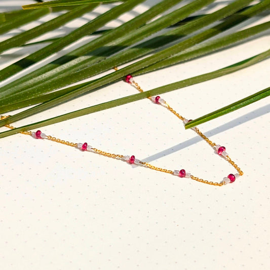 Gold necklace with red beads on a leafy background