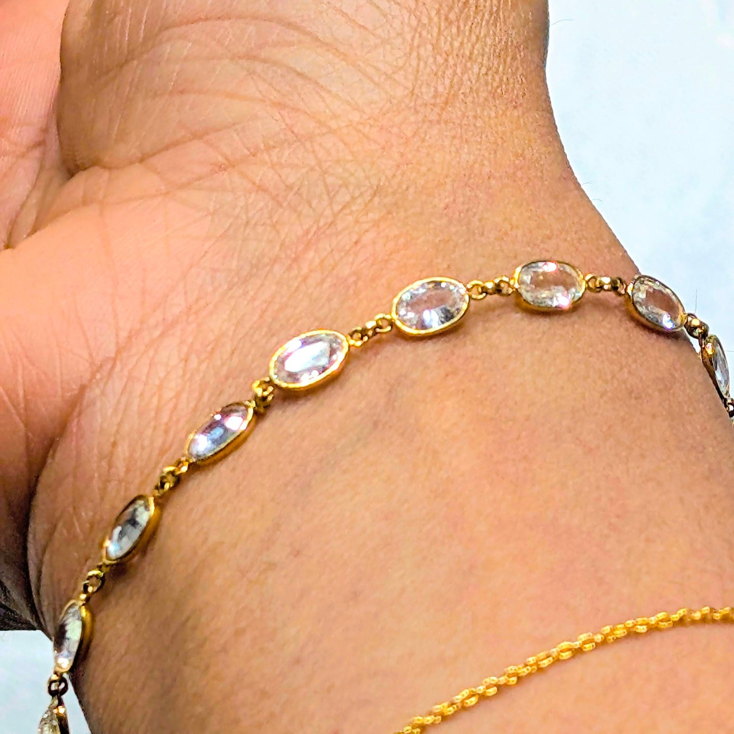 Gold bracelet with clear stones on a wrist against a white background