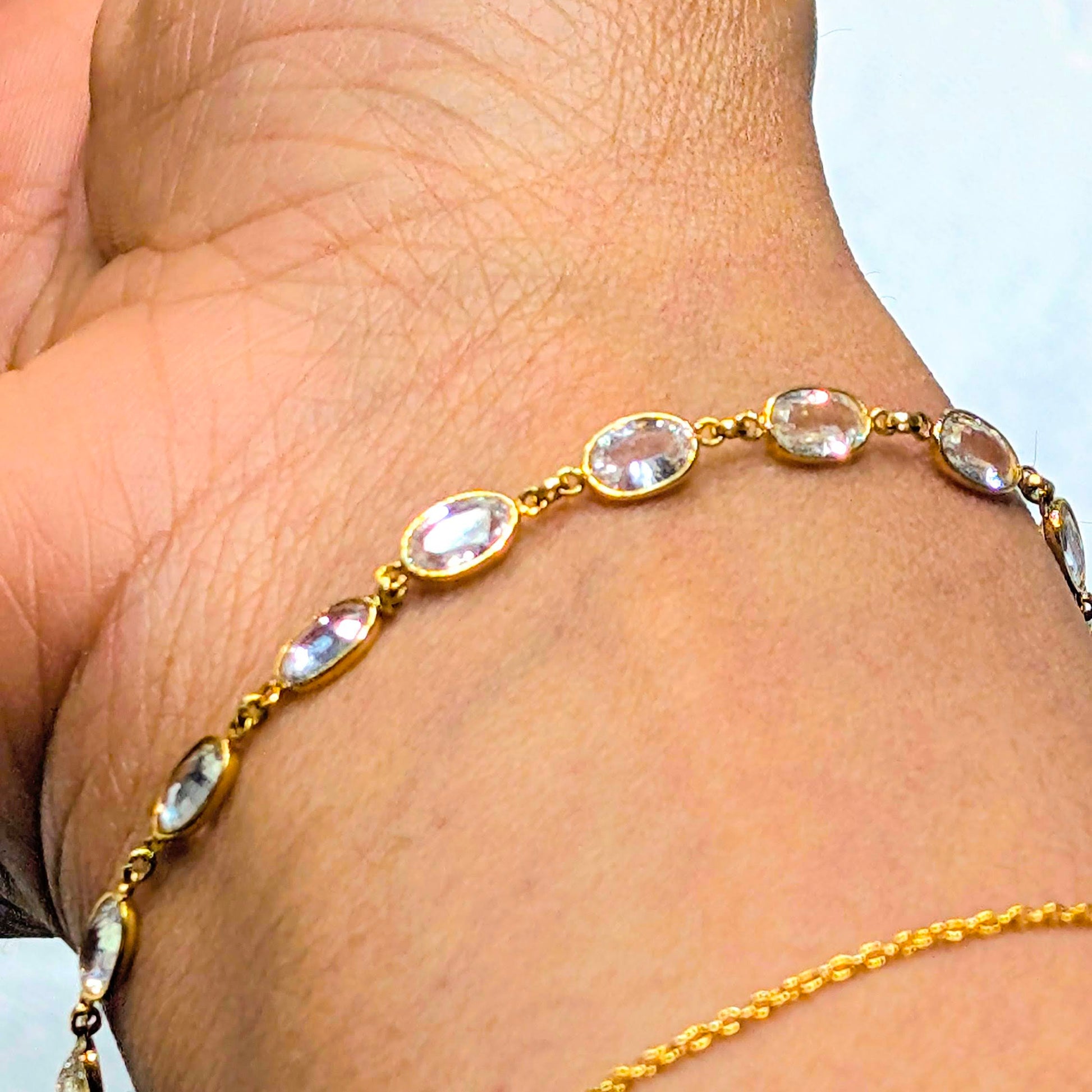 Gold bracelet with clear stones on a wrist against a white background