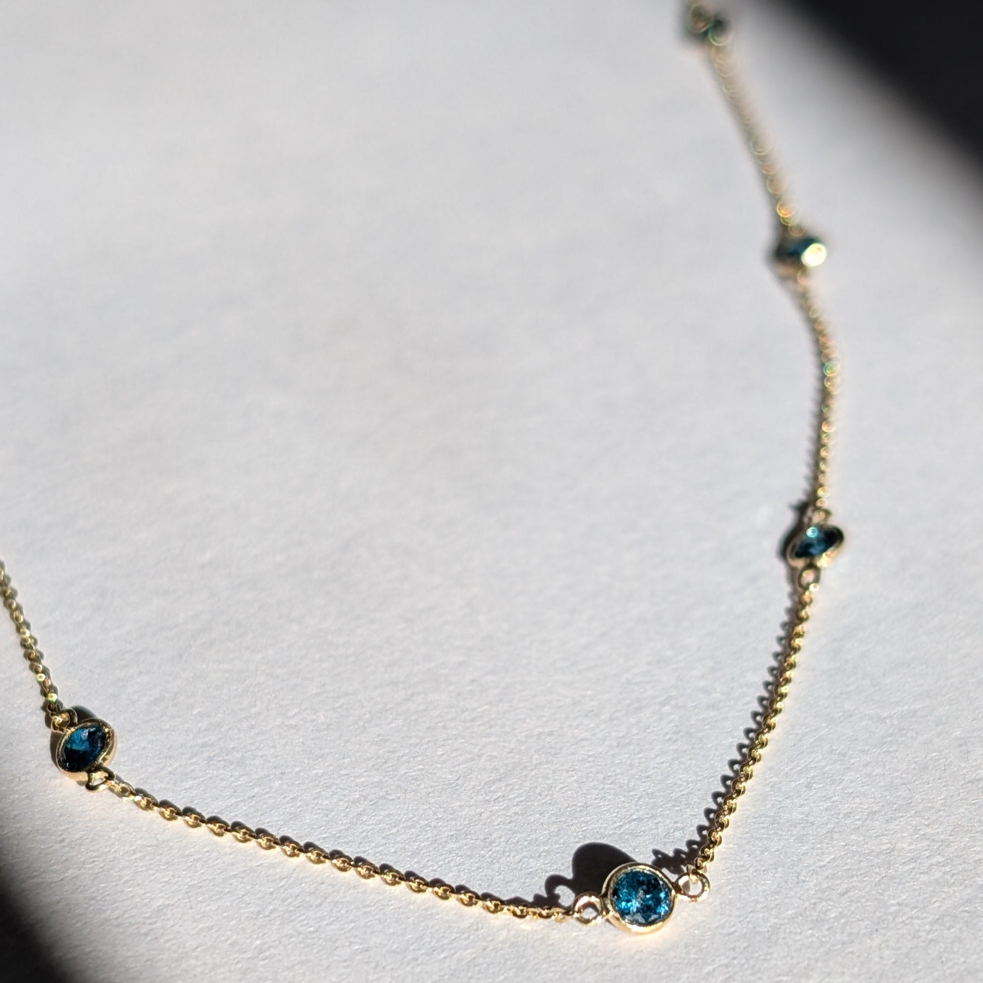 A 14K gold necklace with a series of small blue diamonds set along a longer-length chain.