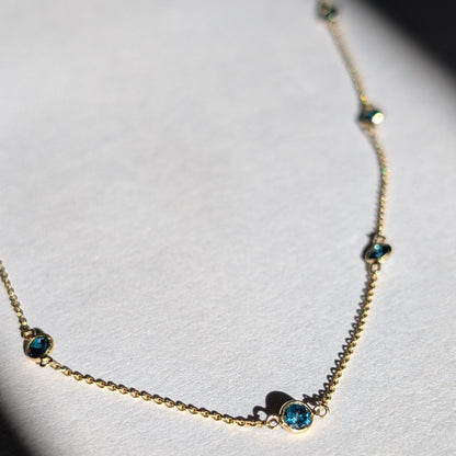 A 14K gold necklace with a series of small blue diamonds set along a longer-length chain.