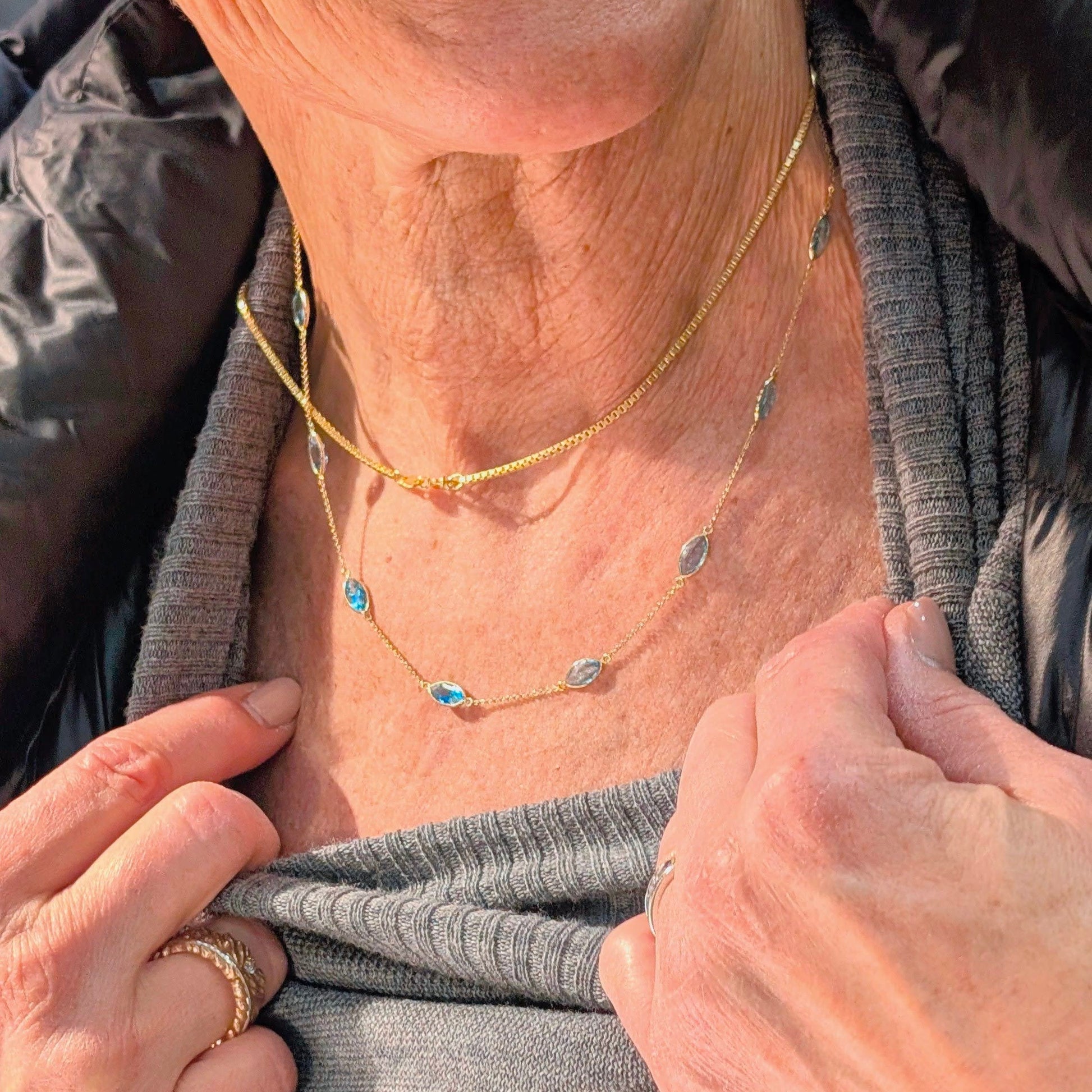 Close-up of a person wearing a gold necklace with small blue stones.