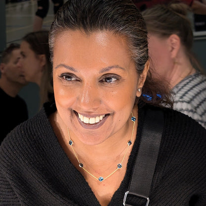 Woman wearing a black sweater wearing London Blue Topaz Necklace with a Prada pouch over her shoulder, smiling.