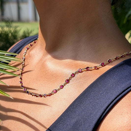Necklace with red gemstones, rhodolites, worn by a person, with a blurred natural background