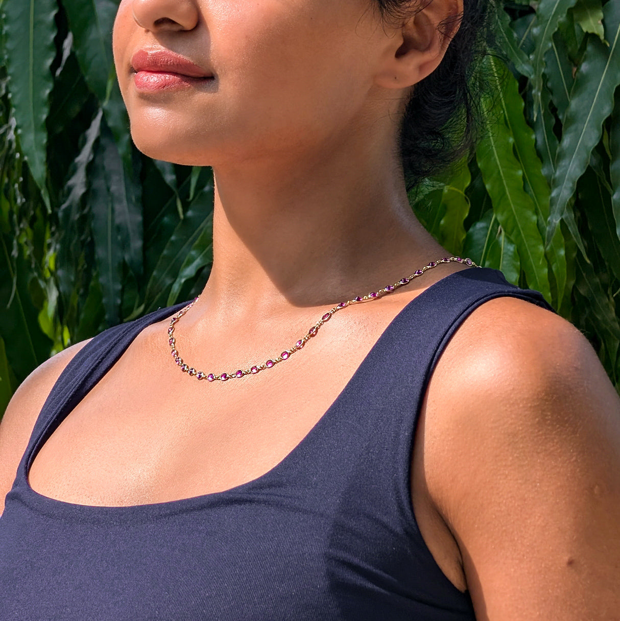 Woman wearing Rhodolite necklace with green foliage in the background