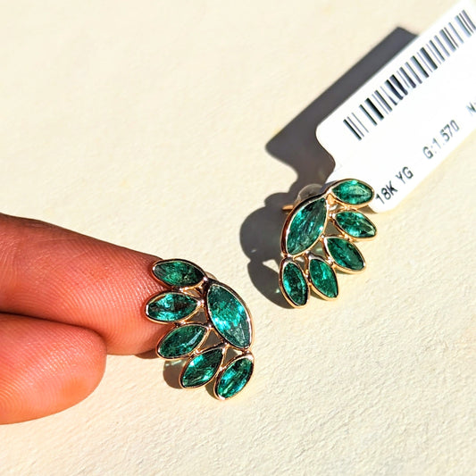 Emeralds earrings held by a hand with a beige background