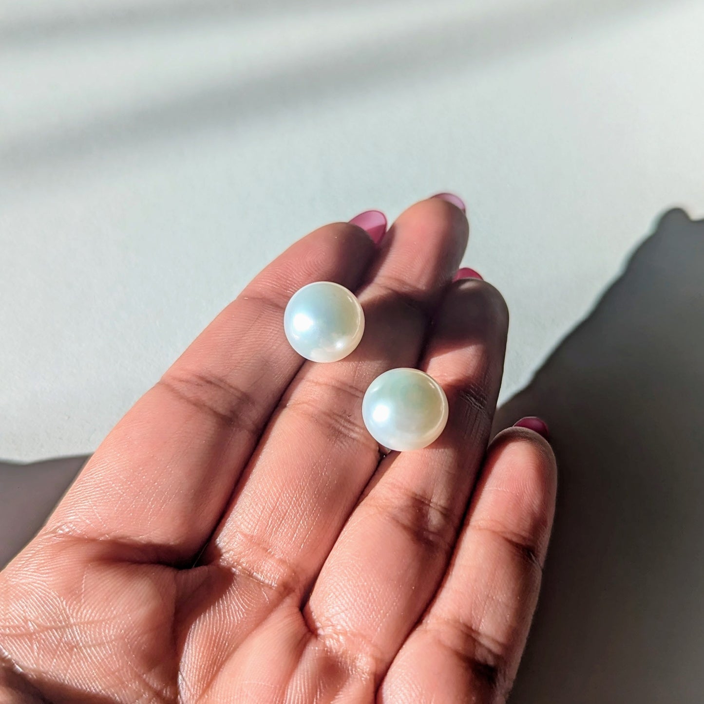 Two pearl earrings held in a hand against a neutral background