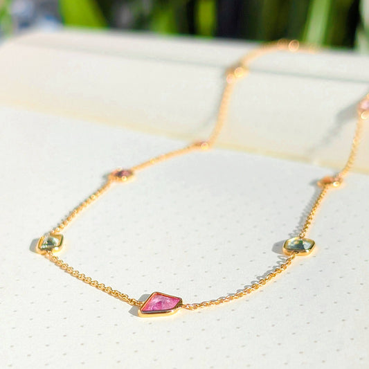 Gold necklace with gemstones on a white cushion with a blurred green background