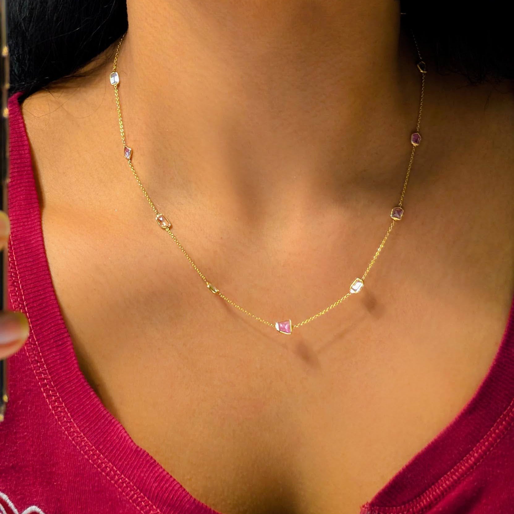 Close-up of a woman wearing a gold necklace with pink stones.