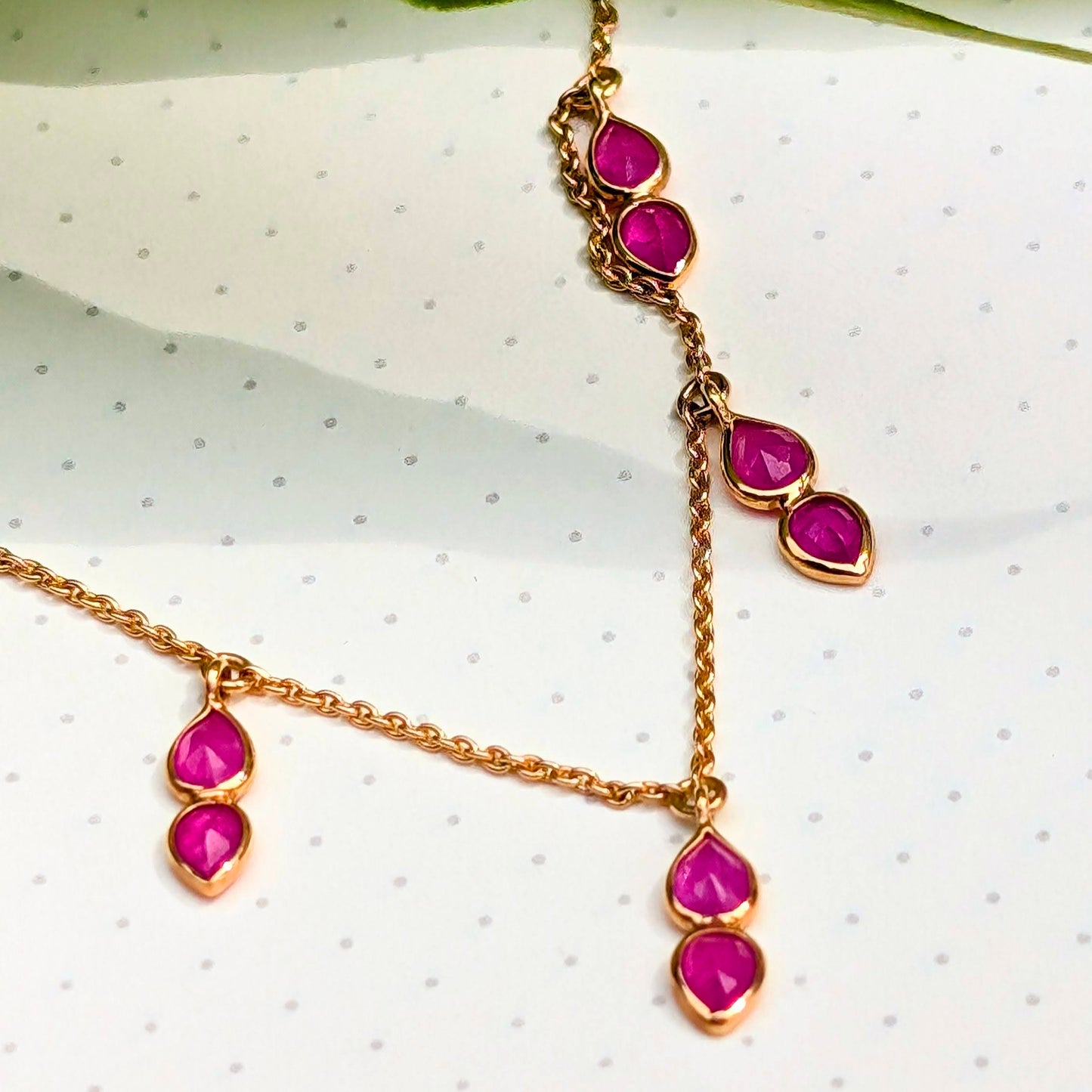 Gold necklace with pink gemstones on a white surface with green leaves.