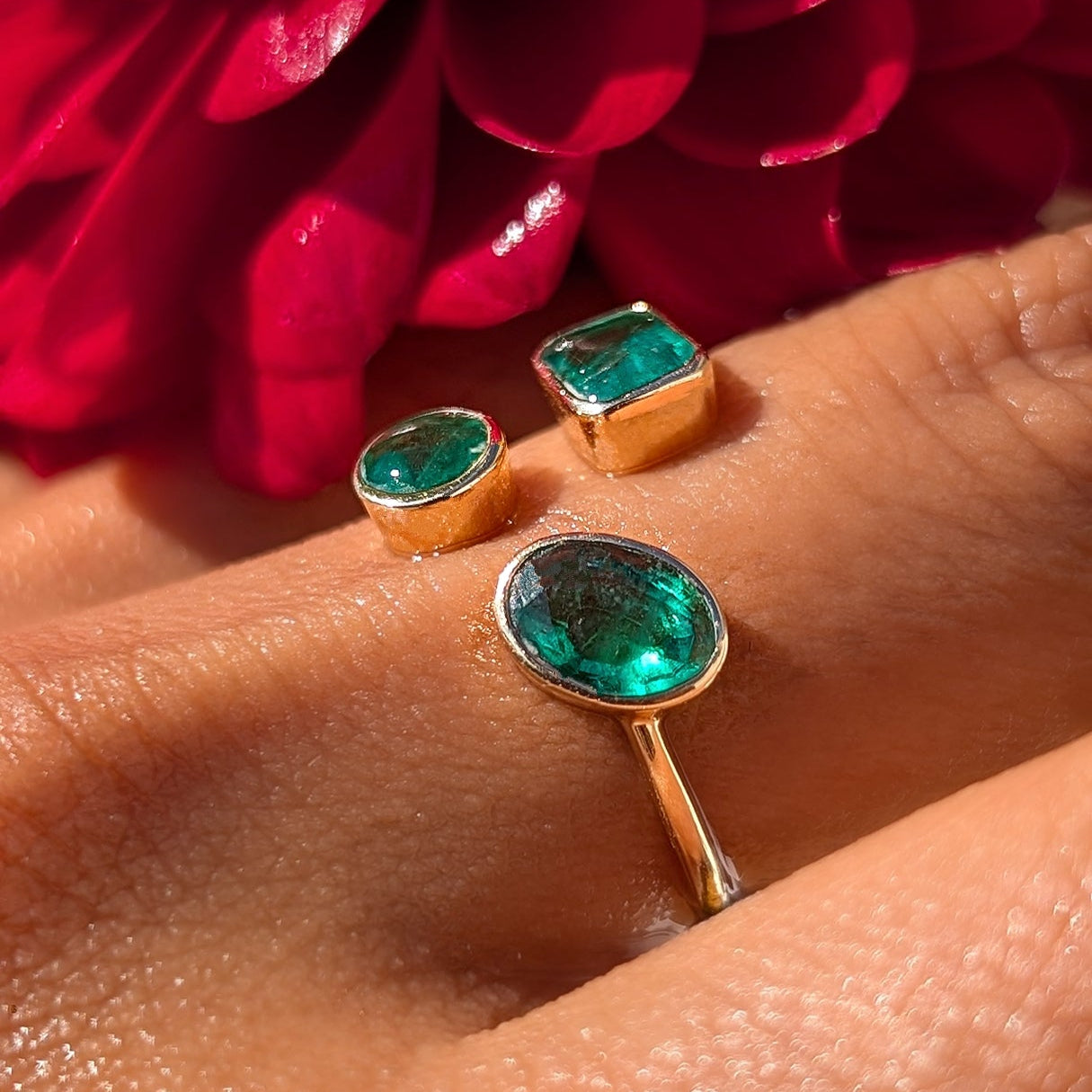 Gold rings with green gemstones on a hand with red flowers in the background