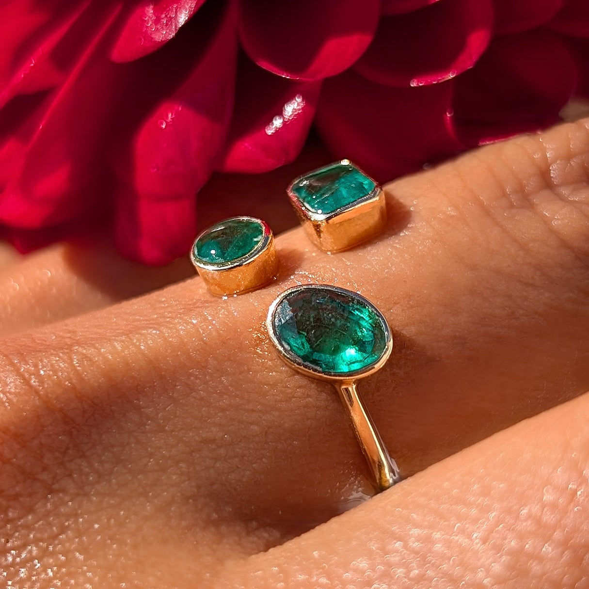 Gold rings with green gemstones on a hand with red flowers in the background