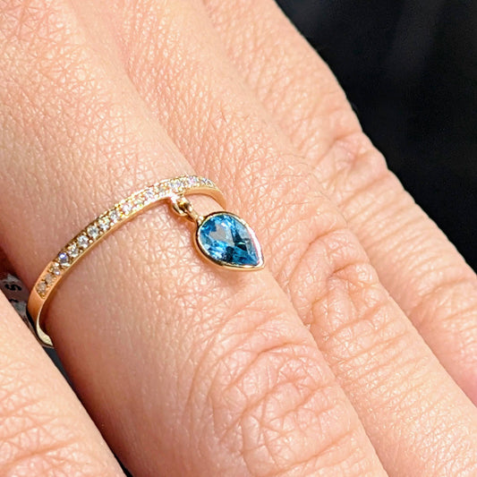 Gold ring with a blue gemstone on a person's finger against a dark background
