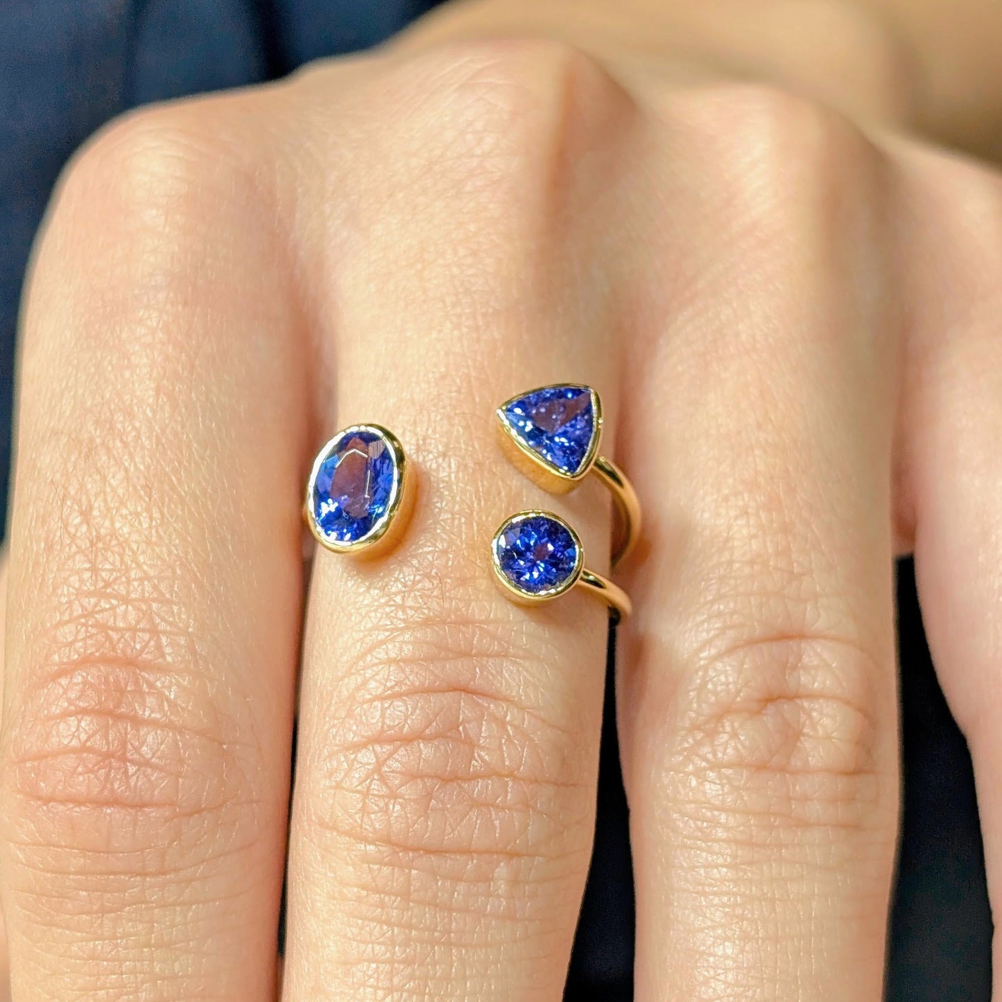 Close-up of a hand wearing two gold rings with blue gemstones on a dark background
