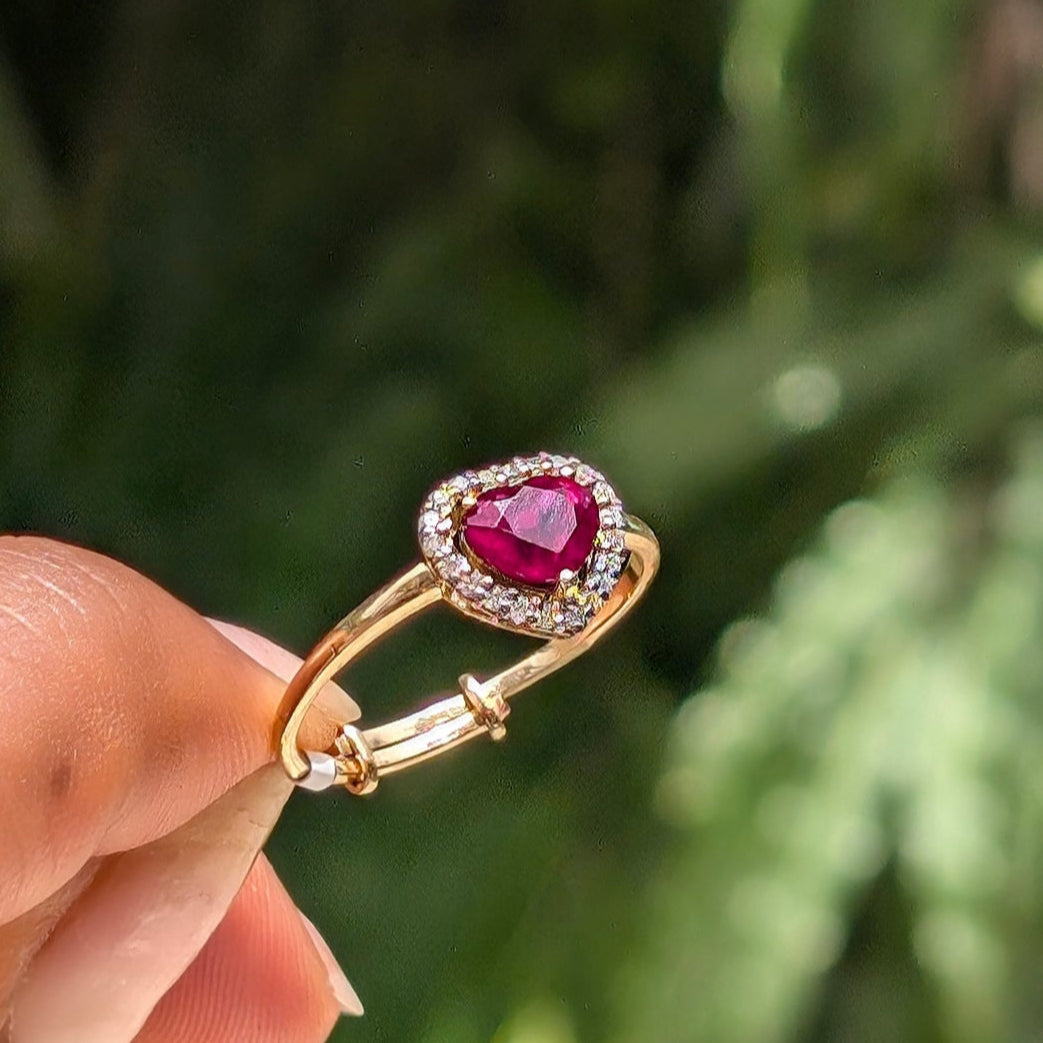 Gold ring with a red gemstone held by a hand against a blurred green background