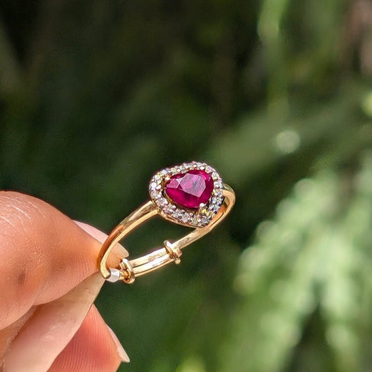 Gold ring with a red gemstone held by a hand against a blurred green background